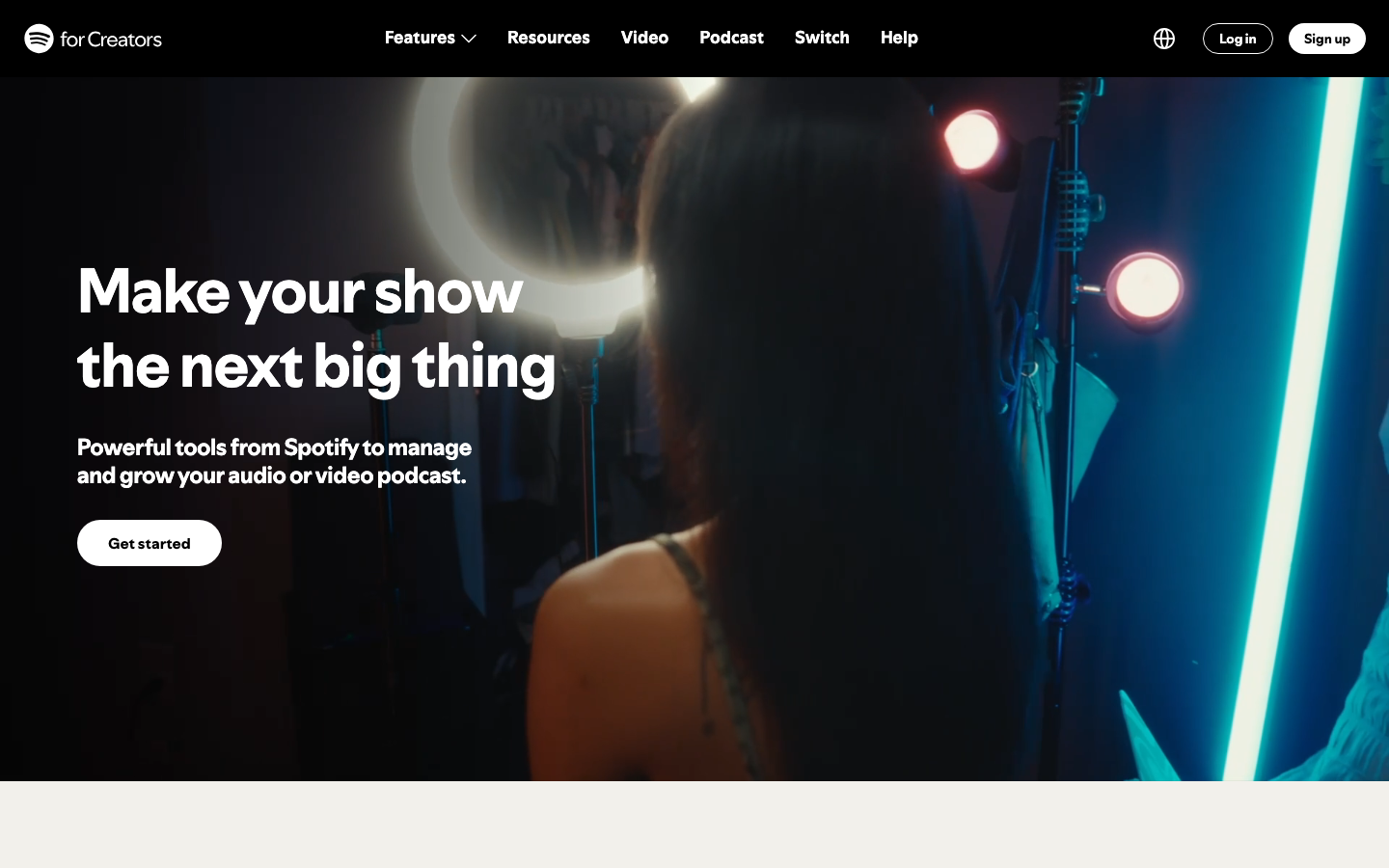 The page uses a stark contrast of deep blues and bright neon accents to highlight the central image of a creator working with audio equipment. The layout is split, with the left side featuring a full-bleed image and the right showcasing text-based information and calls to action. It feels like a behind-the-scenes look at a creative process. · spotify for creators, audio podcast, creator tools, music production, studio workflow, dark interface, neon accents, creative platform, podcast management, audio editing
