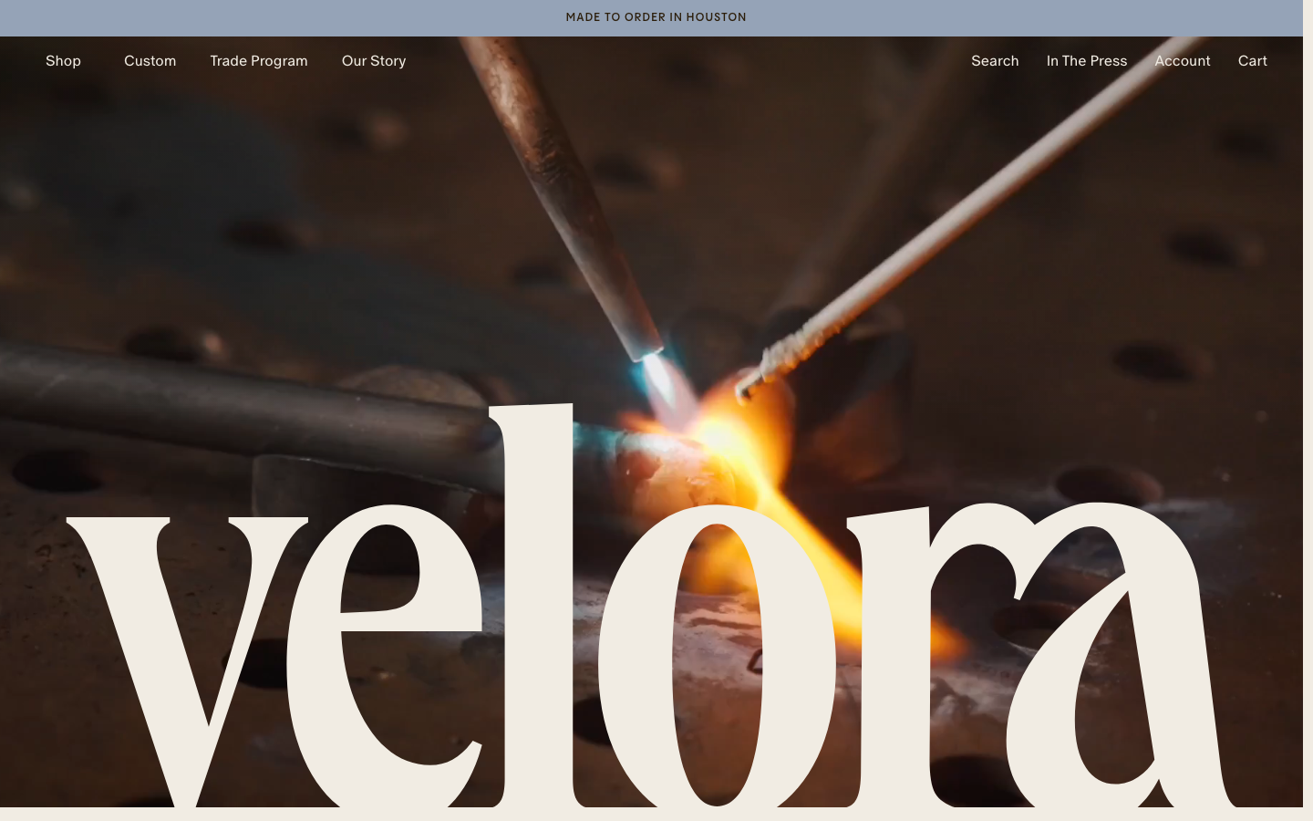High-impact visual composition featuring a massive, overlapping serif typeface set against a cinematic close-up of metal welding. The contrast between the refined typography and the industrial imagery creates a sophisticated, artisanal mood. · luxury lighting hero, industrial editorial design, large serif typography, fullbleed image hero, artisanal ecommerce home